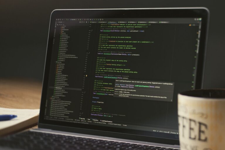 A close-up of a laptop displaying code in a dimly lit room with a coffee mug nearby.