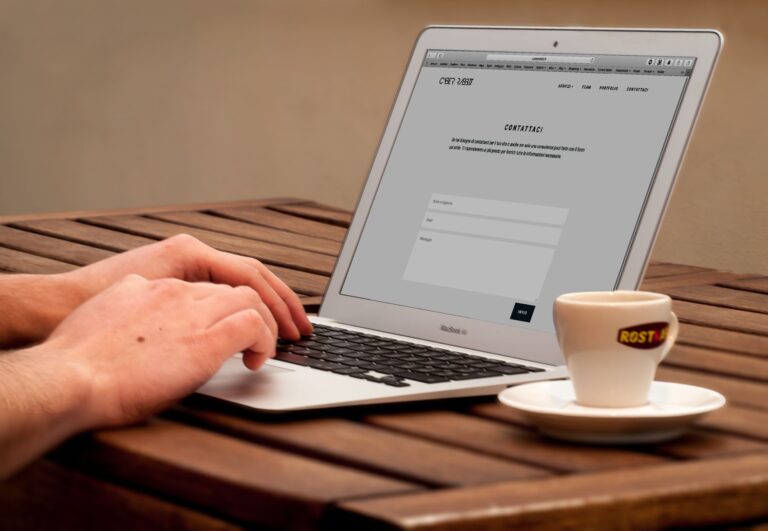 Close-up of hands typing on a laptop next to a cup of coffee on a wooden desk