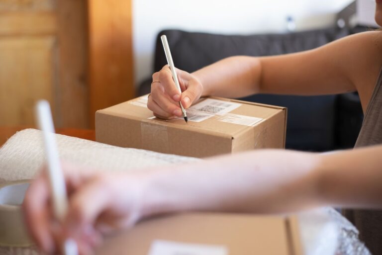 Solo founder hands labeling a packaged order from a home office, symbolizing the first sale of a small product business