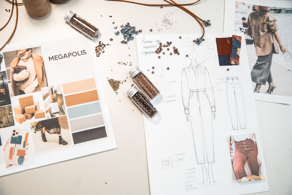 Creative fashion workspace featuring design sketches, mood boards, and beads on a desk.